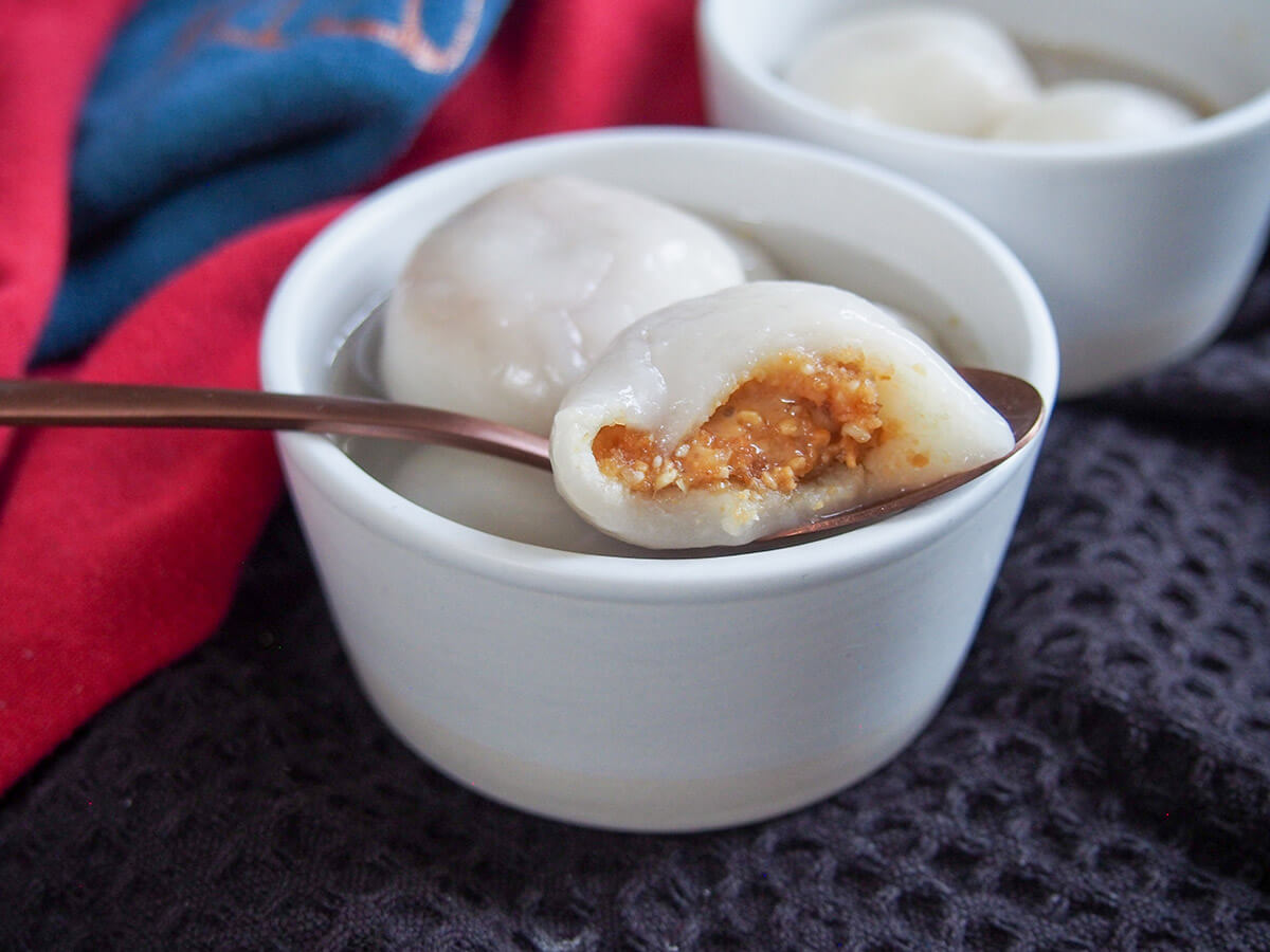 peanut filling showing on Chinese sweet dumplings - tangyuan - resting on bowl with more