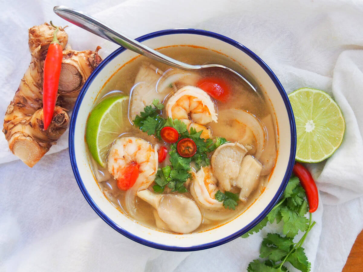 bowl of tom yum soup with spoon in bowl and spices either side of bowl