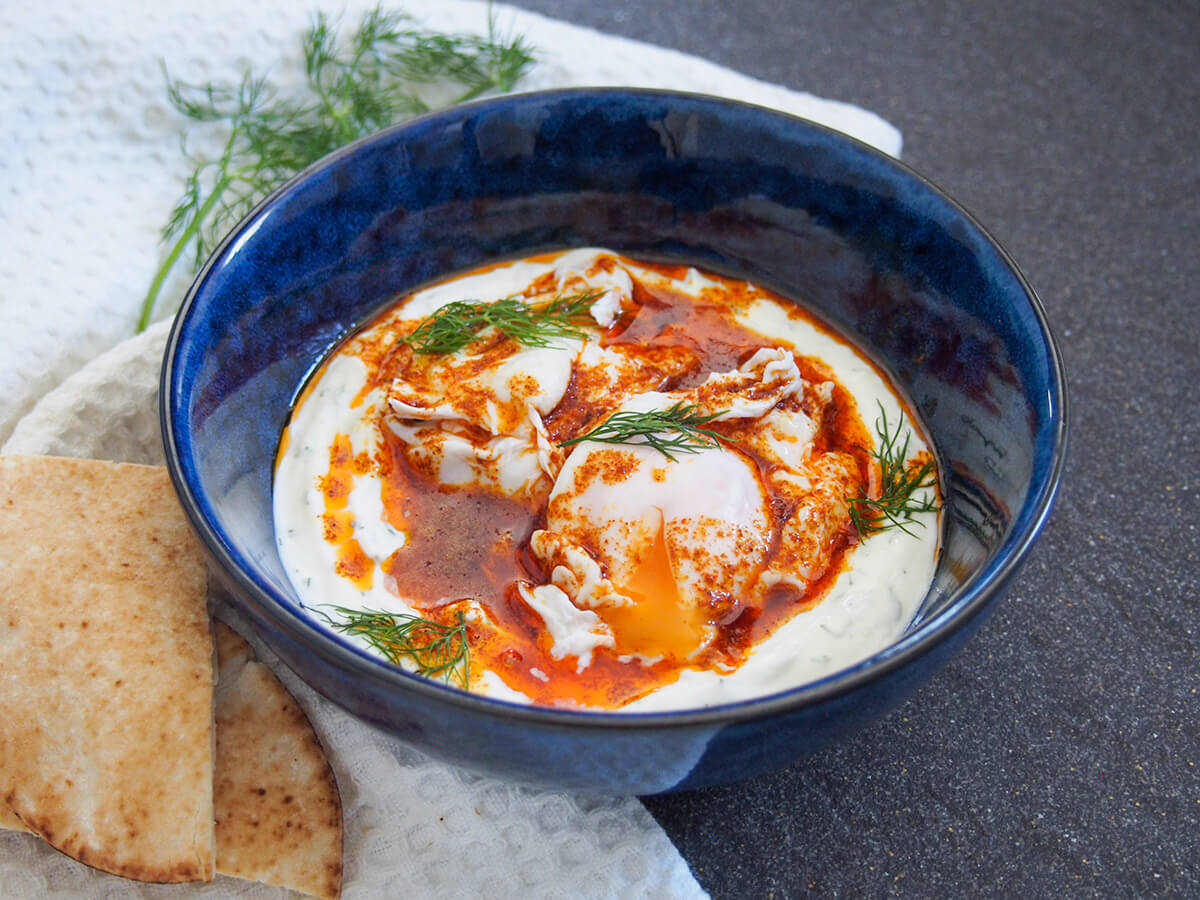 bowl of Turkish eggs cilbir with yolk of front egg leaking into sauce