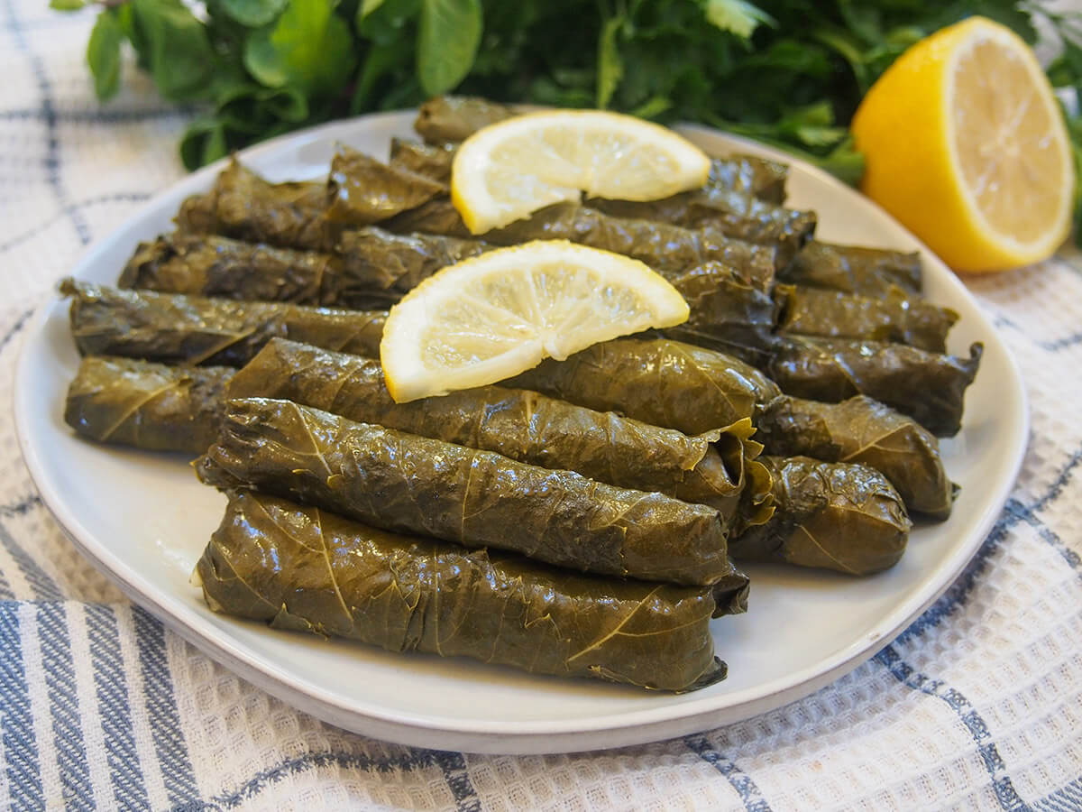 plate of Turkish stuffed grape leaves, yalanci dolma with lemon and herbs behind