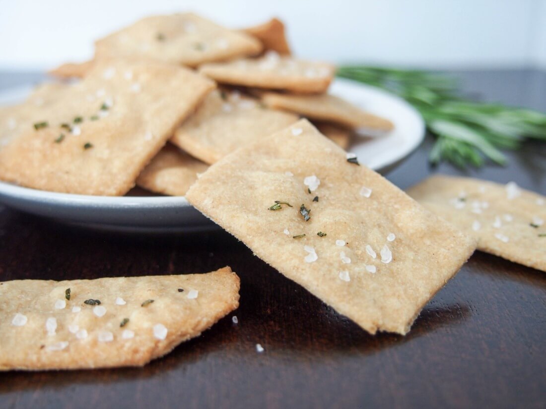 whole wheat olive oil crackers with one sitting on front of plate with crackers stacked on it