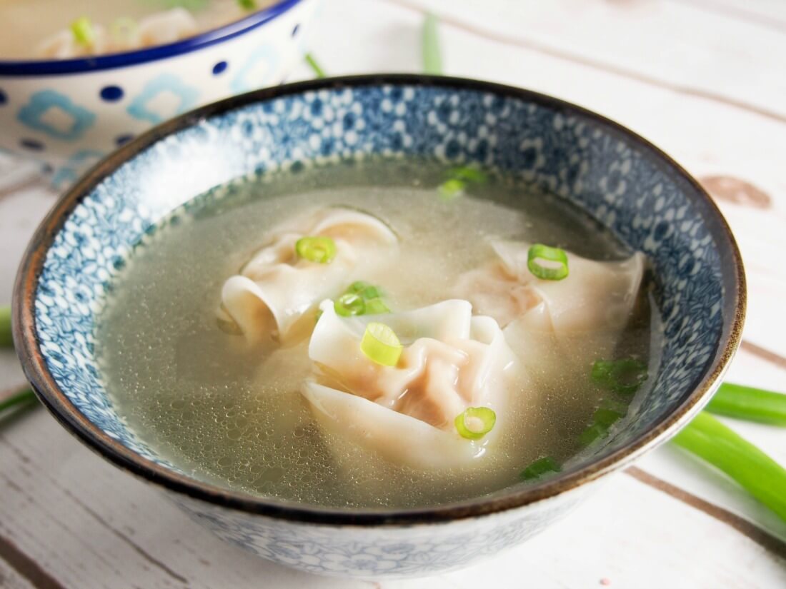 bowl of wonton soup from side with corner of other bowl behind